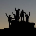 A group in silhouette holding up their arms in victory